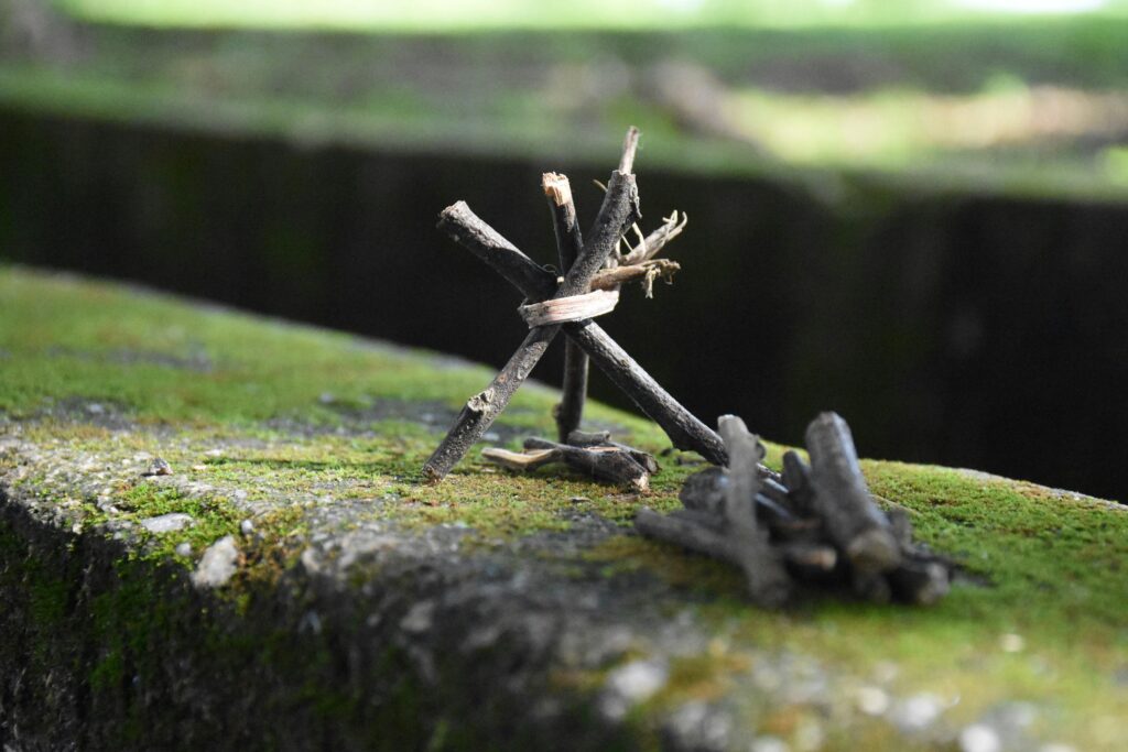 Close-up of a small stick teepee on a moss-covered wall outdoors in daylight.