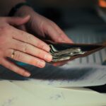 Hands holding an open wallet filled with cash above documents, indicating financial planning or budgeting.
